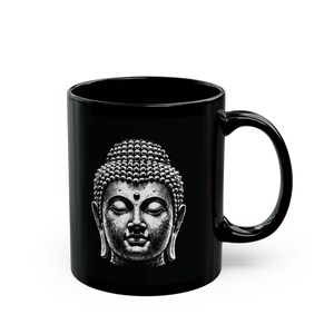 Könnte beinhalten: Schwarze Keramik-Tasse mit einer Graustufen-Illustration eines Buddha-Kopfes. Das Design ist auf der Tasse zentriert und zeigt das ruhige Gesicht und die detaillierten Haare und Gesichtszüge. Die Tasse hat einen Standardgriff.