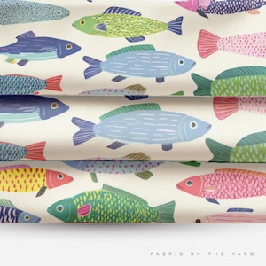May include: A fabric featuring a repeating pattern of stylized fish in various colors including light blue, lime green, pink, yellow, and dark blue on an off-white background. The text FABRIC BY THE YARD is printed in the bottom right corner.