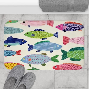 May include: A rectangular bath mat with a repeating pattern of colourful fish in shades of blue, pink, green, and yellow against a cream background. The fish have detailed scales and fins. A pair of grey slippers are in the lower left corner.
