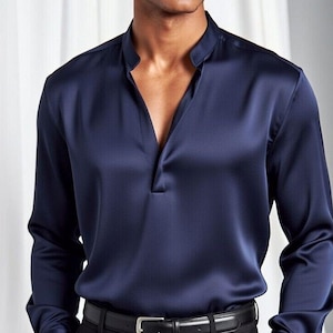 May include: A navy blue satin shirt with a mandarin collar and a V-neck opening. The long-sleeved shirt is paired with black dress pants and a black leather belt with a silver buckle. The outfit is formal wear.