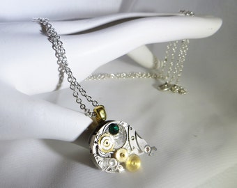 May include: A silver chain necklace with a pendant made from a repurposed watch. The pendant features a green gemstone and gold gears.