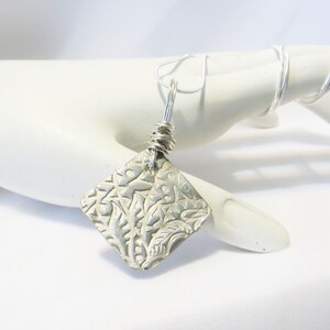 May include: A silver pendant necklace with a square-shaped pendant featuring a detailed embossed floral design. The pendant is attached to a silver chain.