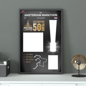 Könnte beinhalten: Ein gerahmtes Poster für den Amsterdam-Marathon, das sein 50-jähriges Jubiläum feiert. Das schwarze Poster zeigt weißen Text und Grafiken, einschließlich des Renndatums, der Distanz (42.195 m) und einer Kartenumriss. Das Poster wird auf einer weißen Oberfläche angezeigt.