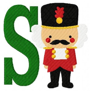 May include: An embroidered design showing a green letter "S" beside a cartoon nutcracker soldier. The nutcracker has a black hat with a red plume, a red jacket, and black trousers. The design has a festive, holiday theme.