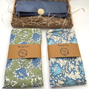 May include: Two rectangular fabric storage pouches featuring floral patterns. The left pouch has green leaves and blue flowers, while the right has cream leaves and blue flowers. Each is wrapped in a brown paper band labelled Storage Pouch Texart by Sarah.