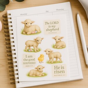 Puede incluir: Una agenda blanca con una espiral dorada. La agenda tiene una variedad de pegatinas con imágenes de corderos y versículos bíblicos. Los versículos incluyen "El Señor es mi pastor", "Yo soy el buen pastor" y "Ha resucitado".