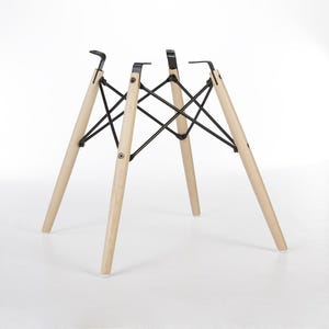 May include: A set of four wooden chair legs with black metal supports. The legs are light-colored wood, angled outwards, and connected by a black metal frame. The chair legs are designed for a modern aesthetic.