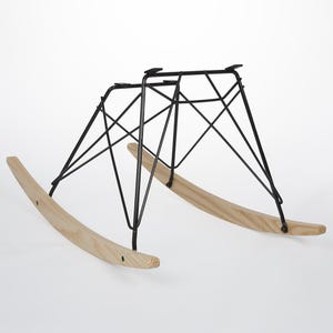 May include: A black metal rocking chair base with a geometric design. The base is paired with two curved, light-colored wooden rockers. The design is modern and minimalist, suitable for various chair styles.