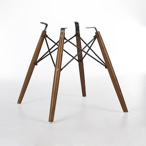 May include: A set of four wooden chair legs with a dark brown finish. The legs are connected by a black metal support structure. The legs are angled outward and have a modern design.
