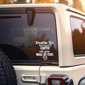 Può includere: Adesivo in vinile bianco applicato al finestrino di un'auto. Il testo recita "Breathe Sis. this is just a CHAPTER not your WHOLE LIFE STORY." con un cuore. L'auto è bianca.
