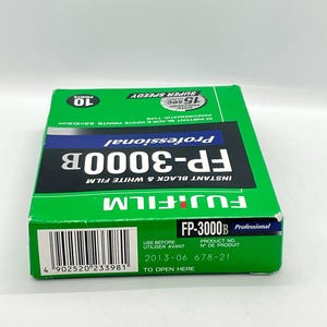 Peut inclure: Une bo&icirc;te de film noir et blanc instantan&eacute; Fujifilm FP-3000B verte et noire. La bo&icirc;te pr&eacute;sente le texte "Professional", "Super Speedy" et "10 Prints". La bo&icirc;te comprend &eacute;galement le texte "Instant Black & White Prints 6,5 x 10,8 cm".