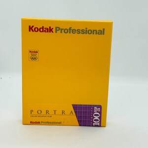 May include: A yellow rectangular box of Kodak Professional Portra 100T color negative film. The box features the text Kodak Professional, a Kodak Worldwide Sponsor Olympic logo, and a purple grid graphic with the text 100T.