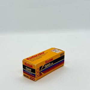 May include: A rectangular box of Kodak Gold 200 film. The box is primarily orange with black, red, and blue stripes. Text on the box includes "Kodacolor," "Kodak Gold Film," and "GB 120 200." The film is for color prints.