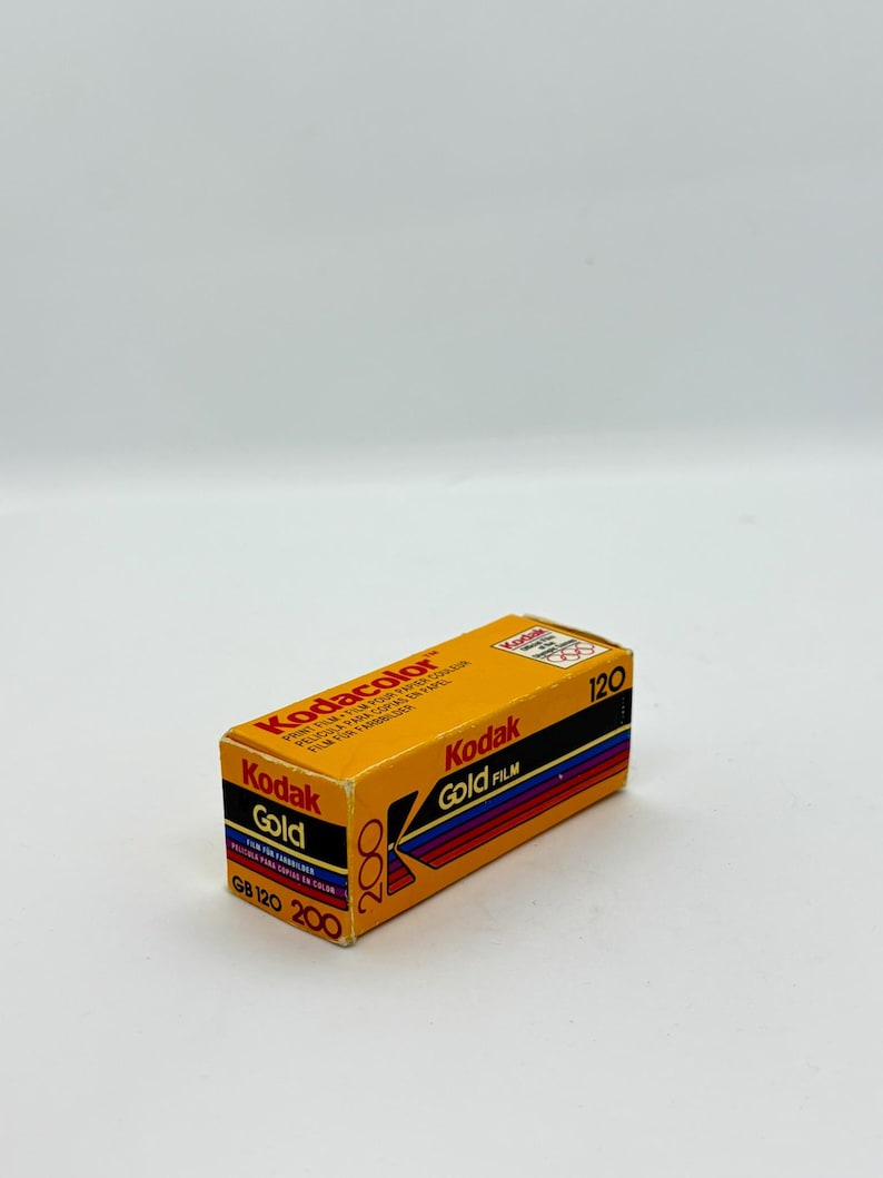 May include: A rectangular box of Kodak Gold 200 film. The box is primarily orange with black, red, and blue stripes. Text on the box includes "Kodacolor," "Kodak Gold Film," and "GB 120 200." The film is for color prints.