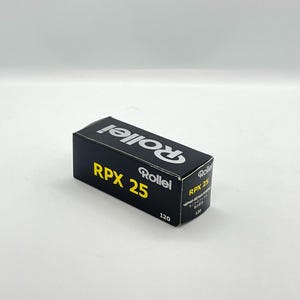 May include: A black box of Rollei RPX 25 film, with the brand name and product details in white and yellow. The box is labeled "120" and includes text in multiple languages.