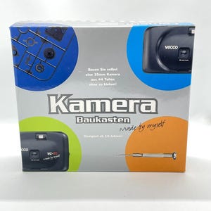 Op de afbeelding: Een camerakitdoos met het woord "Kamera" in grote letters. De doos heeft een zwarte camera-afbeelding, de tekst "Made by myself" en de tekst "Bouw zelf een 35mm camera uit 44 onderdelen zonder te lijmen!"