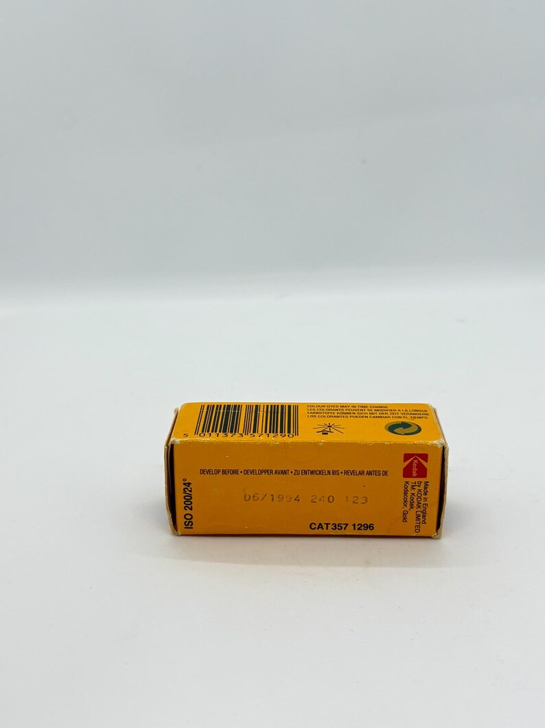 May include: A small, rectangular Kodak film box in yellow and black. The box has text that reads "ISO 200/24", "DEVELOP BEFORE", and "06/1994". The film box is a vintage item.