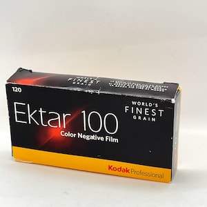 Könnte beinhalten: Eine Schachtel mit Kodak Ektar 100 Farbnegativfilm. Die Schachtel ist schwarz mit orangefarbenen und gelben Akzenten und trägt den weißen Schriftzug "Ektar 100". Die Schachtel trägt auch den Text "World's Finest Grain" und "Kodak Professional".