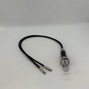Può includere: Cavo di scatto per fotocamera nero e argento con pulsante argentato. Il cavo ha due estremità argentate. L'accessorio fotografico è su sfondo bianco.