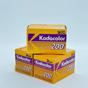 Puede incluir: Tres cajas amarillas y moradas de película Kodacolor 200. Cada caja presenta el logotipo de Kodak, el texto Kodacolor 200 e indica 36 exposiciones. El empaque incluye líneas horizontales y texto que especifica que la película es para copias en color.