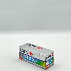 May include: A silver and blue Agfa RSX II 120 film box. The box has the Agfa logo and the text "RSX II 100 PROFESSIONAL 120". The box is rectangular and has a silver, blue, and green gradient.