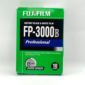 Peut inclure: Bo&icirc;te de film noir et blanc instantan&eacute; Fujifilm FP-3000B verte. La bo&icirc;te affiche le logo Fujifilm, les informations sur le produit et le texte "10 tirages noir et blanc instantan&eacute;s 8,5 x 10,8 cm". Elle indique &eacute;galement un temps de traitement de 15 secondes.