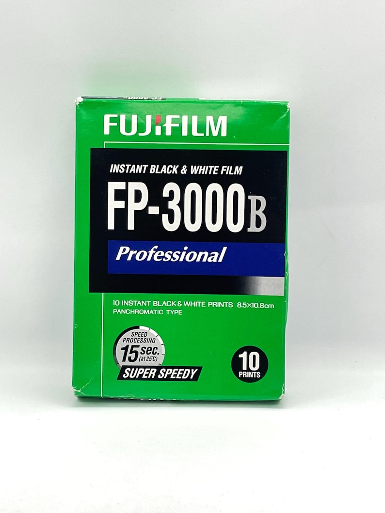 Peut inclure: Bo&icirc;te de film noir et blanc instantan&eacute; Fujifilm FP-3000B verte. La bo&icirc;te affiche le logo Fujifilm, les informations sur le produit et le texte "10 tirages noir et blanc instantan&eacute;s 8,5 x 10,8 cm". Elle indique &eacute;galement un temps de traitement de 15 secondes.