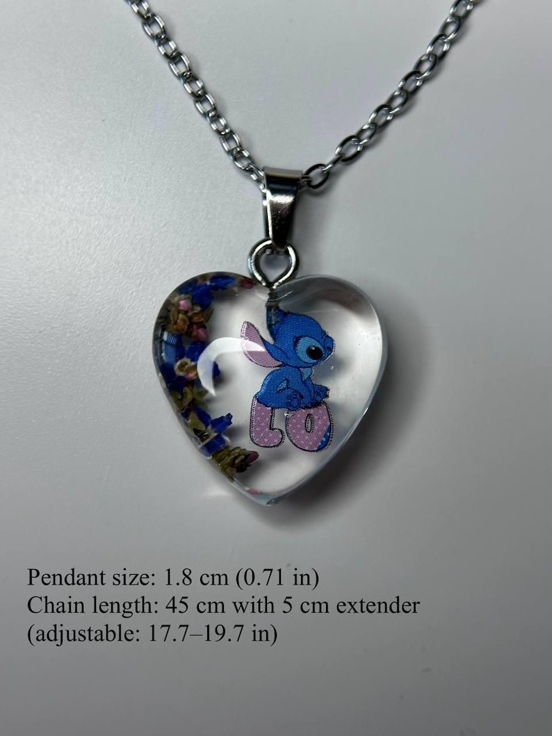 Puede incluir: Collar con colgante en forma de coraz&oacute;n con un dise&ntilde;o de resina transparente. El colgante presenta un personaje de dibujos animados azul y flores secas. La cadena es plateada. Tama&ntilde;o del colgante: 1,8 cm. Longitud de la cadena: 45 cm.