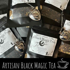 May include: Black Magic Tea packages with heart-shaped tea infusers. The tea bags are black with white labels featuring a crescent moon and raven design. The text "Artisan Black Magic Tea" is at the bottom.