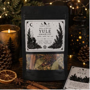 Könnte beinhalten: Ein schwarzer Standbeutel mit der Aufschrift Roaming Raven Wheel of the Year Yule Simmer Pot. Das Etikett zeigt einen Kessel, Tannenzweige und Text, der Zutaten wie Orangenscheiben, Zimt, Nelken, Sternanis, Kiefernnadeln und Zedernholz auflistet.