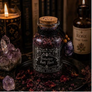 May include: A clear glass jar filled with dark purple bath salts, sealed with a cork stopper. The label features white text reading Seduction Bath Spell. A black cord is wrapped around the neck, adorned with wooden beads and a purple crystal pendant.