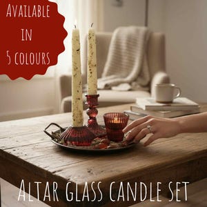 May include: A decorative altar glass candle set on a wooden table. The set includes two lit candles in red glass holders, a small votive candle, and a decorative tray. The text "AVAILABLE IN 5 COLOURS" is visible.