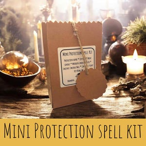 Puede incluir: Una bolsa de papel marrón con la etiqueta "Mini Protection Spell Kit" y una lista de contenido. Una pequeña etiqueta redonda marrón cuelga de la bolsa. El fondo incluye velas y otros objetos místicos.