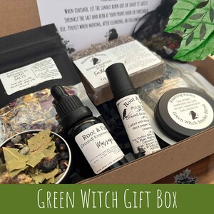 May include: A gift box with various items, including a bottle of massage oil, a roller bottle, a tin of Green Witch Smoke Blend, a bar of soap, and a bag of botanical bath salts. The box is labeled "Green Witch Gift Box".