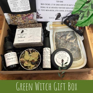 May include: A gift box filled with various self-care items. Includes botanical bath salts, handcrafted soap, massage oil, pulse roller, tea, and a blend. The box is labeled "Green Witch Gift Box".