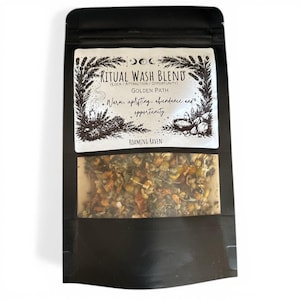 May include: A black pouch with a clear window displaying a blend of herbs and flowers. The label reads "RITUAL WASH BLEND" with the subtext "GOLDEN PATH" and "Warm, uplifting, abundance and opportunity." The brand name "ROAMING RAVEN" is also visible.