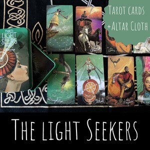以下が含まれることがあります： 「The Light Seer's Tarot」と書かれた緑色の金属製の箱に入ったタロットカードと祭壇布のセット。カラフルなイラストが描かれたタロットカードがいくつか表示されています。「TAROT CARDS + ALTAR CLOTH」と「THE LIGHT SEEKERS」の文字も表示されています。