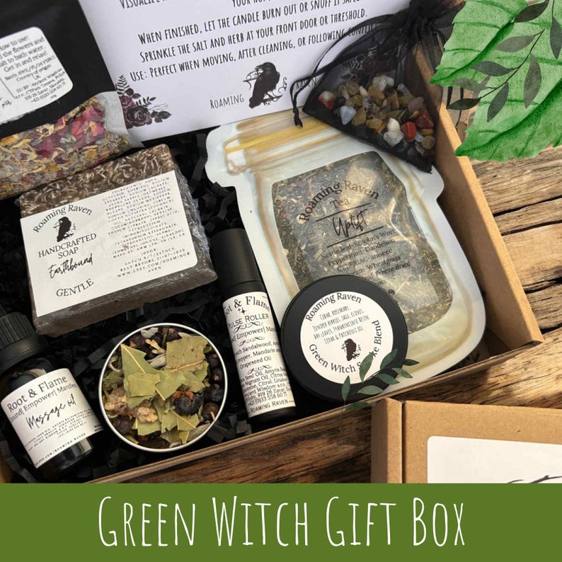 May include: A wooden gift box filled with various items, including handcrafted soap, tea, massage oil, and a blend. The box features the text "Green Witch Gift Box" and branding from "Roaming Raven."