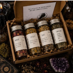 May include: A cardboard gift box containing four glass jars filled with dried herbs and flowers. The labels read Amoure, Lucidity, Solace, and Sanctum. A white card inside the box features the text, The cycles of the moon remind me that change is sacred.