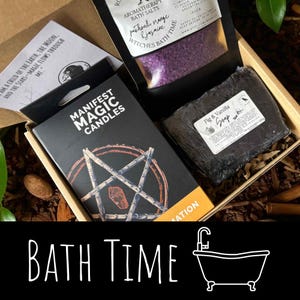 May include: A gift box with bath products, including a box of "Manifest Magic Candles", a bag of purple bath salts, and a bar of "Fig & Vanilla Soap". The box also contains a card with text. The words "BATH TIME" are written in white at the bottom.