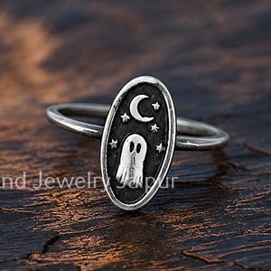 Op de afbeelding: Een zilveren ring met een ovaalvormig blad waarop een geest, een maansikkel en kleine sterren zijn gegraveerd. Het metaal heeft een geoxideerde afwerking om de details van de hemelse en spookachtige afbeeldingen op de ring te benadrukken.
