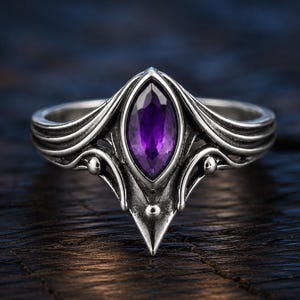 Puede incluir: Un anillo de plata con una amatista morada de corte marquesa en el centro. La banda de metal muestra líneas de plata intrincadas, fluidas y en relieve, con pequeños acentos esféricos que se extienden desde el engaste central de la piedra.