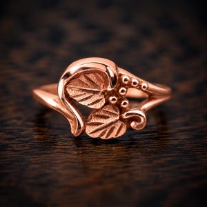 Puede incluir: Un anillo de oro rosa que presenta un dise&ntilde;o central de dos hojas texturizadas y un grupo de peque&ntilde;as cuentas esf&eacute;ricas. La banda es lisa y se estrecha hacia la parte posterior, con el motivo de hojas integrado en el engaste con curvas.