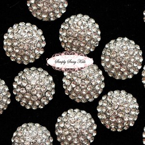 May include: A collection of 12 silver rhinestone embellishments, each featuring a round shape and a cluster of small rhinestones. The embellishments are arranged on a black background.