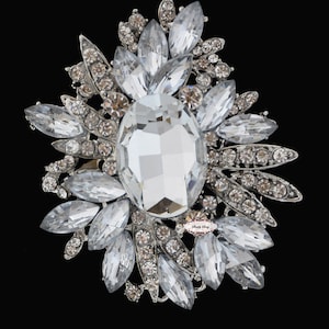 May include: A large silver brooch with a large clear crystal in the center surrounded by smaller clear crystals and silver leaves.