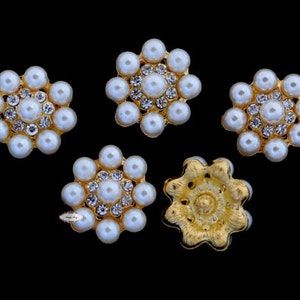 May include: Five gold-toned embellishments with a pearl and rhinestone design. Four of the embellishments are flower-shaped with a central pearl surrounded by smaller pearls and rhinestones. The fifth embellishment is a star-shaped design with a central gold-toned design.