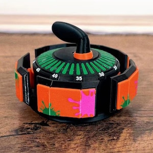 May include: A black and orange timer with a green dial and a black handle. The timer has a series of orange panels with green and pink paint splatters. The dial has numbers from 30 to 45.