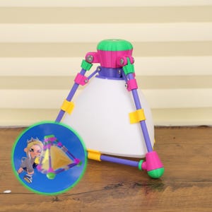 May include: A colorful, geometric tripod with a white conical base, purple legs, and green, pink, and yellow accents. A small, circular inset shows a cartoon character and a miniature pyramid.