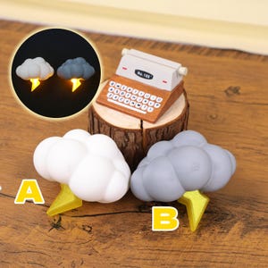 May include: A collection of miniature decorative items, including two cloud-shaped lights with yellow lightning bolts, a miniature typewriter, and two cloud-shaped figurines with lightning bolts. The typewriter is brown and white, and the clouds are white and gray.