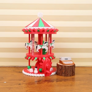 May include: A decorative red and white carousel with green detailing, featuring white horses. The carousel has a striped roof and festive decorations. A miniature typewriter sits on a wooden base, adding a vintage touch.